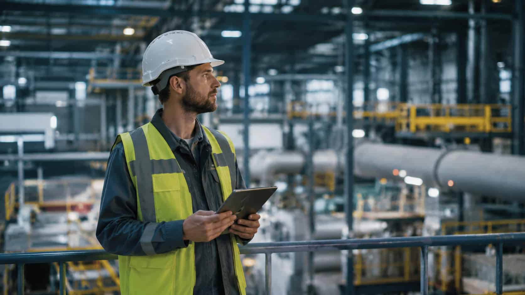Industrial engineer using a tablet inside a factory facility for connected infrastructure monitoring.