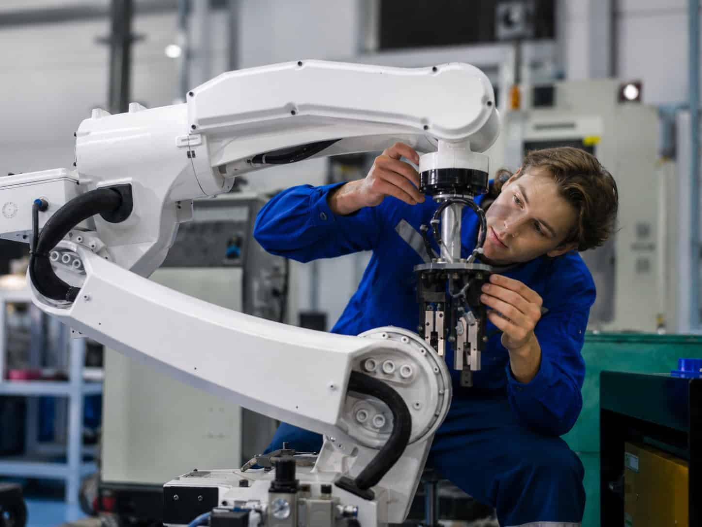 Technician inspecting and adjusting a robotic arm inside an industrial workshop.