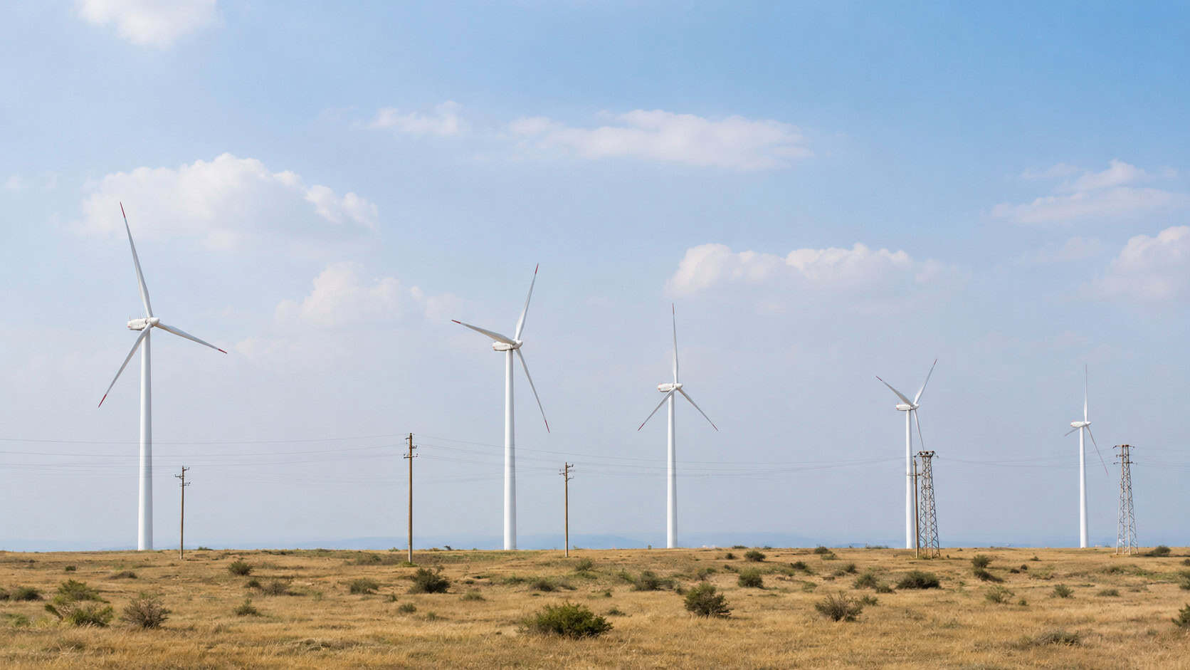 Wind turbines operating across a remote rural landscape with utility infrastructure supporting renewable energy generation.