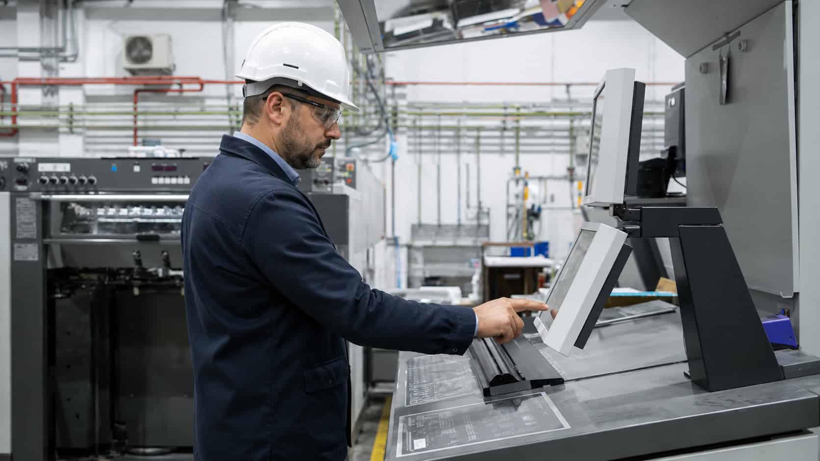 Industrial engineer operating a touchscreen control panel to monitor manufacturing equipment in a modern production facility.