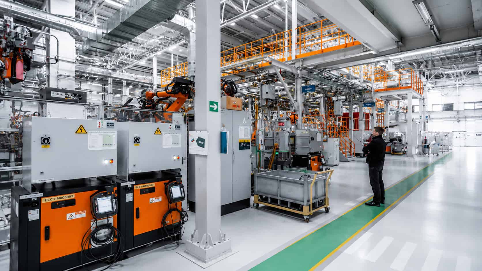 Modern automated factory floor with robotic arms, control equipment, and an engineer reviewing production systems.