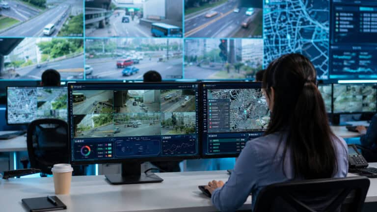 Security operator monitoring multiple surveillance video feeds and real-time analytics from a centralized control room for industrial site management.