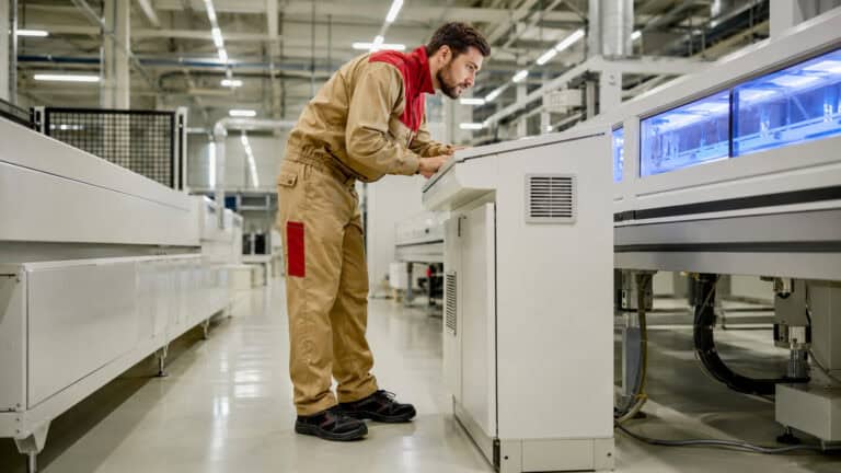Factory technician inspecting an automated industrial machine on a modern production line, with advanced manufacturing equipment, clean workshop surroundings, and industrial automation systems in the background.