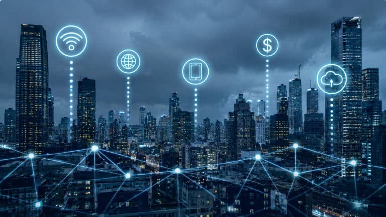 Nighttime city skyline with glowing digital network connections and smart city icons, including Wi-Fi, cloud, mobile device, and global connectivity symbols, representing urban IoT infrastructure and connected smart city technology.