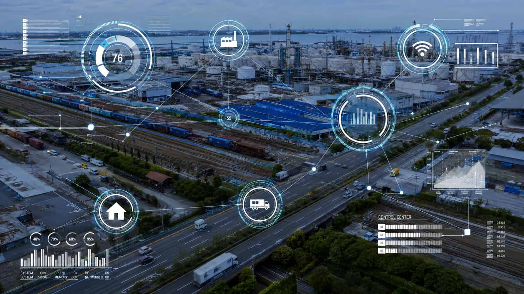 Aerial view of a large industrial facility and logistics hub with warehouses, storage tanks, railways, and highways, overlaid with futuristic digital HUD graphics showing connected systems, data analytics, IoT monitoring, and smart infrastructure management.