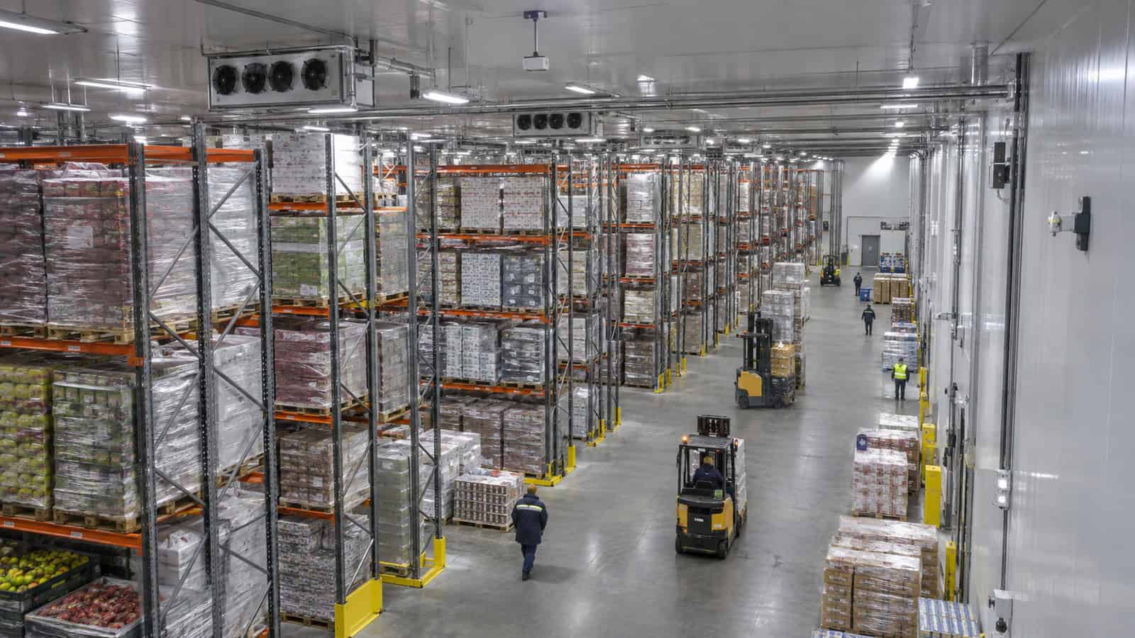 Large refrigerated warehouse with dense racking, ceiling infrastructure and distant workers.
